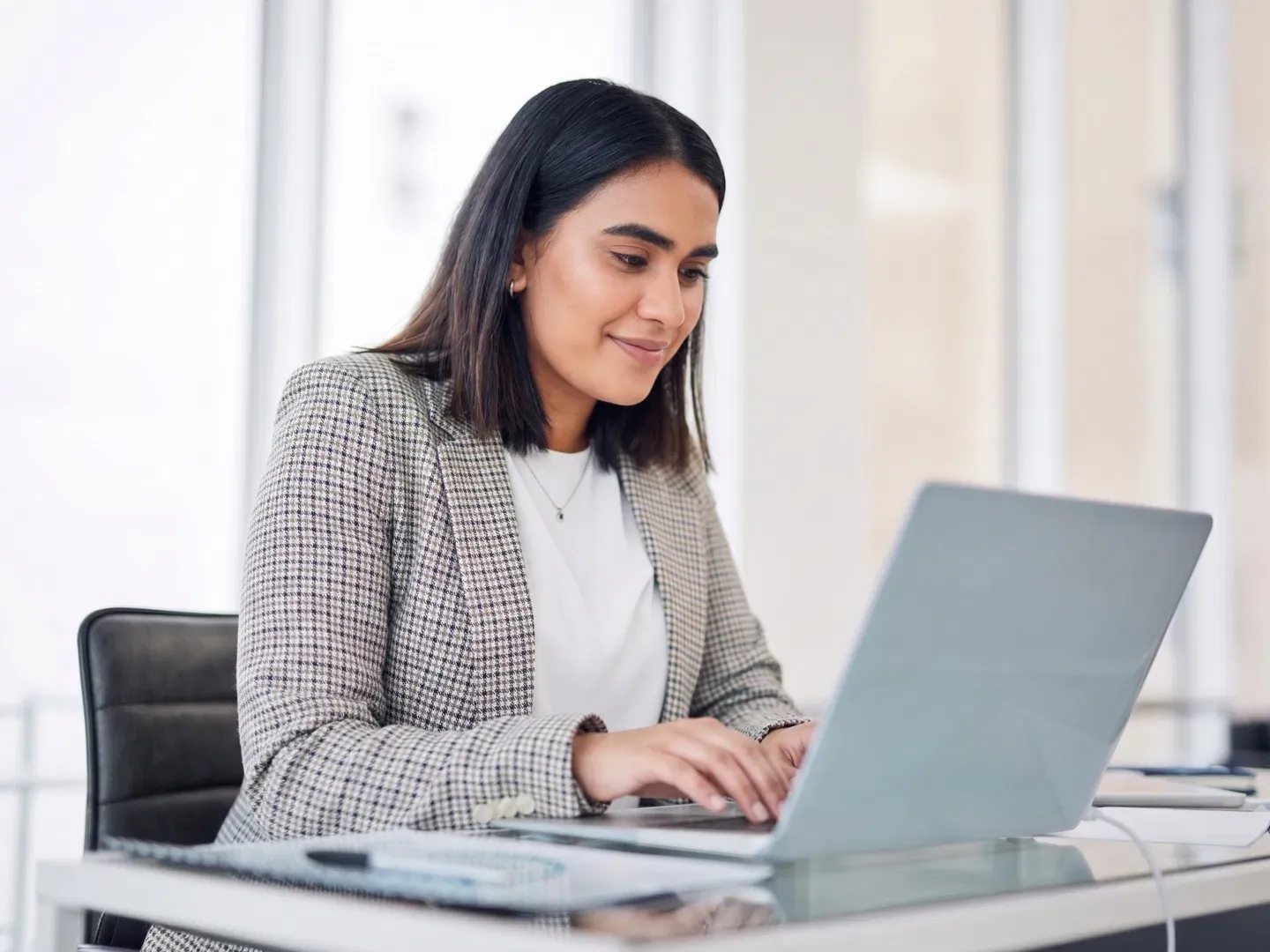 Female Office Worker wearing an adorable plaid blazer, and testing her business' internet speed on her laptop.